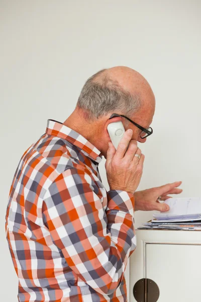 Senior man die met draagbare telefoon in woonkamer. — Stockfoto