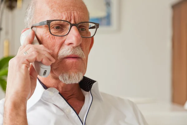 Senior man die met draagbare telefoon in woonkamer. — Stockfoto