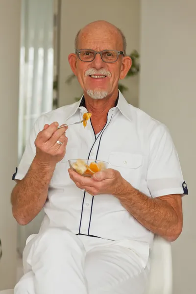 Senior man eten van verse fruitmand. vergadering in woonkamer. — Stockfoto
