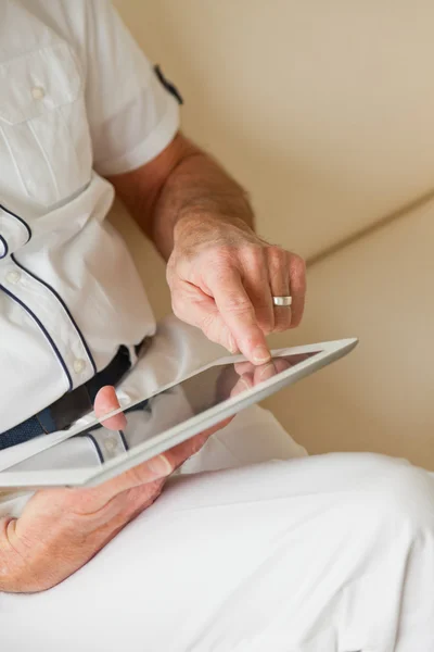 Mãos de homem sênior usando tablet. Sentado no sofá branco . — Fotografia de Stock