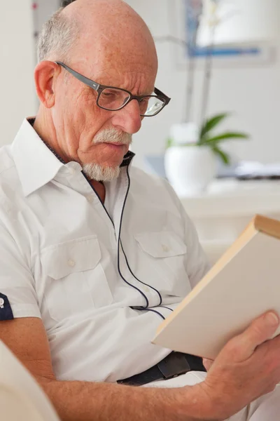 Старший мужчина в очках читает книгу в гостиной . — стоковое фото