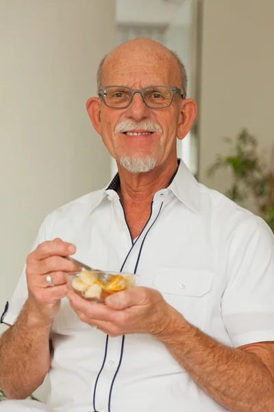 Senior man eten van verse fruitmand. vergadering in woonkamer. — Stockfoto