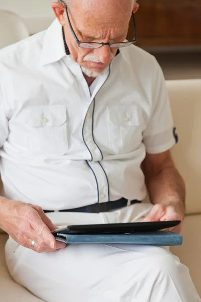 Homme âgé avec des lunettes en utilisant une tablette sur le canapé dans le salon . — Photo