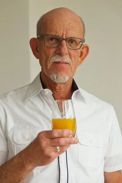 Старший мужчина в очках пьет апельсиновый сок в гостиной . — стоковое фото