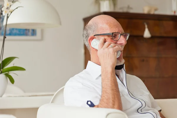 Senior man die met draagbare telefoon in woonkamer. — Stockfoto
