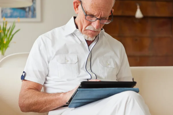Homme âgé avec des lunettes en utilisant une tablette sur le canapé dans le salon . — Photo