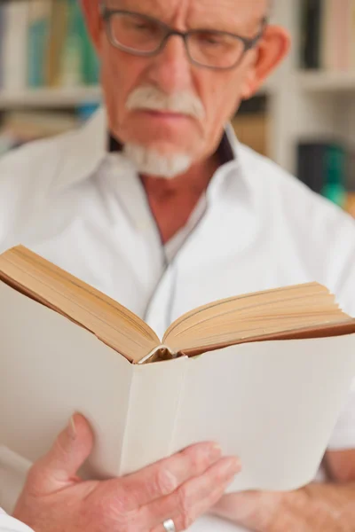 Homem sênior com óculos livro de leitura na frente da estante . — Fotografia de Stock