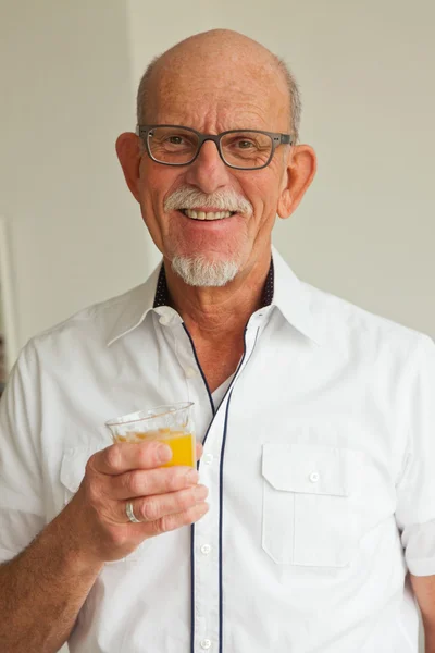 Senior man with glasses drinking orange juice in living room. — Stock Photo, Image