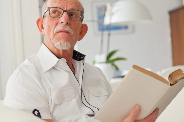 Senior mit Brille liest Buch im Wohnzimmer. — Stockfoto