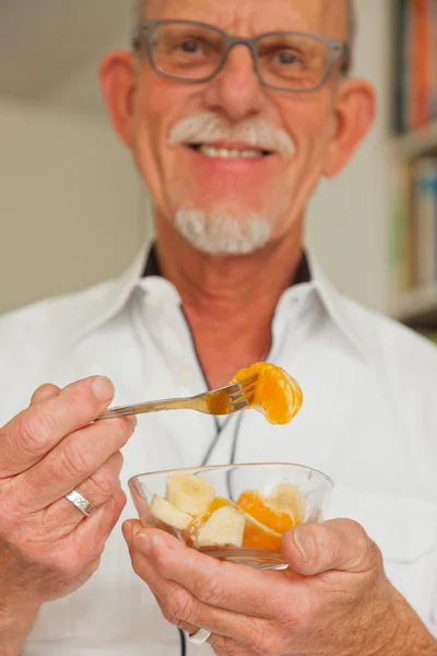 Senior mannen äter färsk frukt maträtt. sitter i vardagsrummet. — Stockfoto