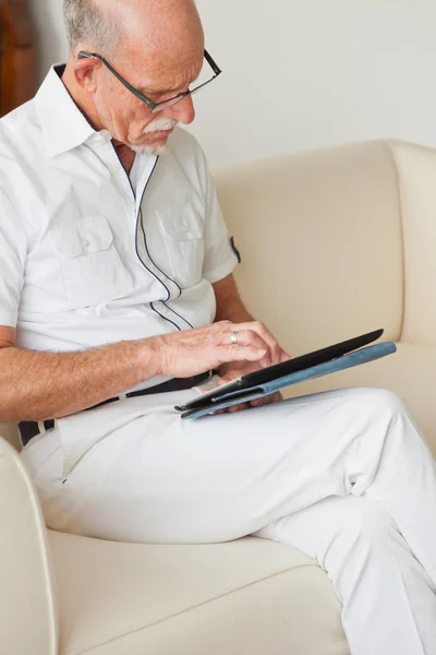 Homme âgé avec des lunettes en utilisant une tablette sur le canapé dans le salon . — Photo