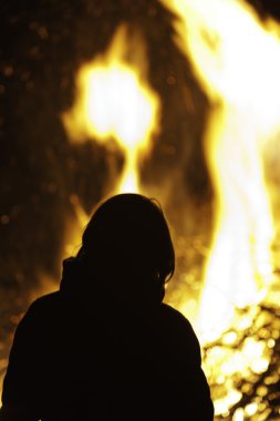 Silhouette of person in front of big campfire. clipart