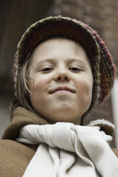 Rolig ung pojke med långt hår och hatt utomhus framför bygga — Stockfoto