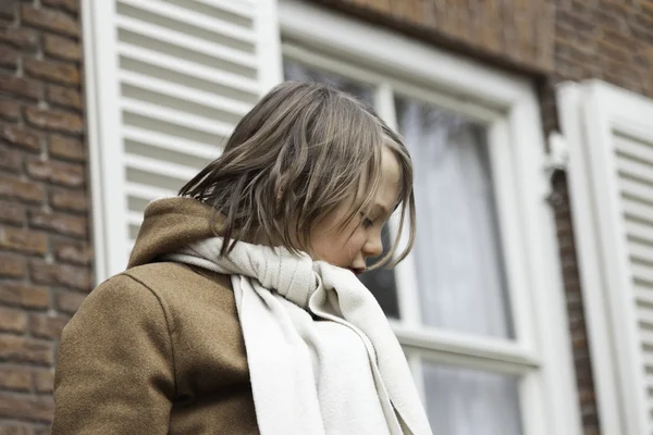 Jeune garçon drôle ludique avec les cheveux longs en plein air devant la construction — Photo