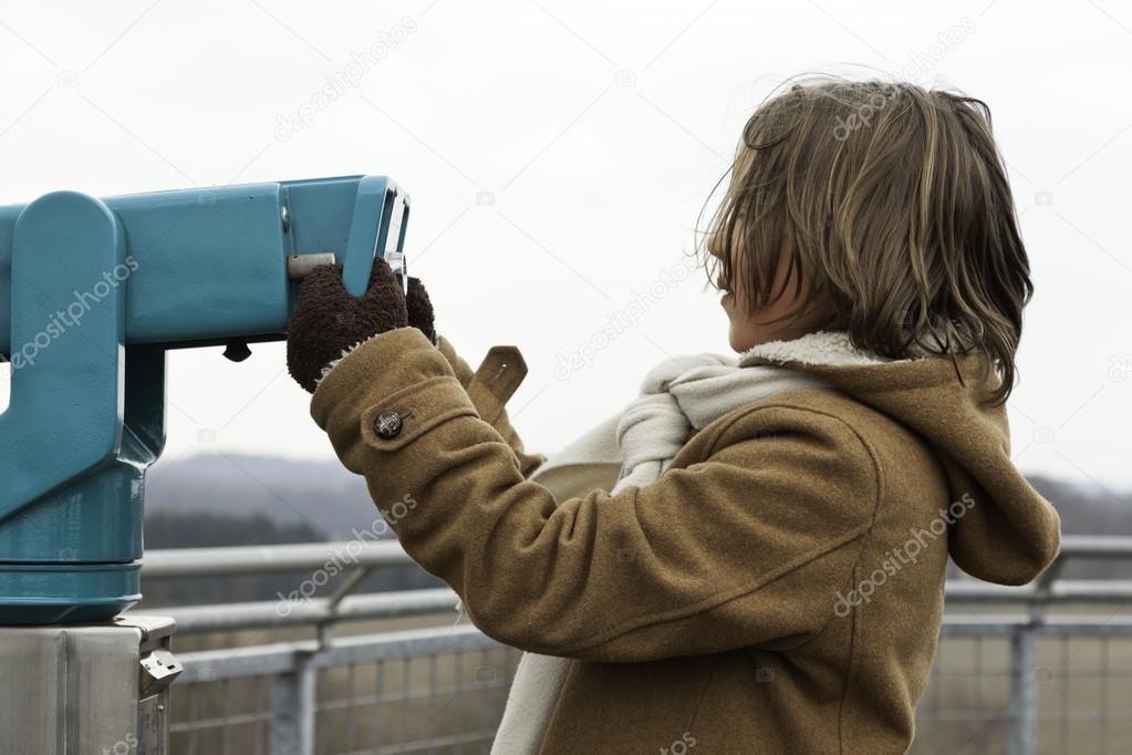 Playful funny young boy with long hair holding telescope.