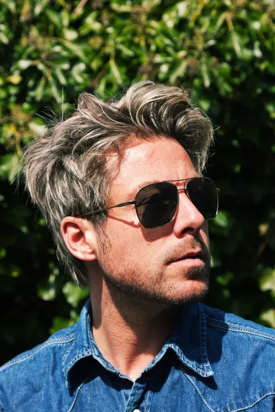 Man with blonde hair in front of green foliage. Wearing sunglass — Stock Photo, Image