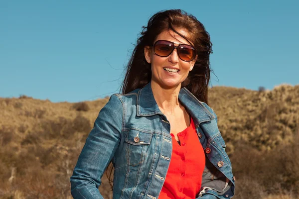 Hübsche brünette Frau mit Jeans und Sonnenbrille. Wiese mit — Stockfoto