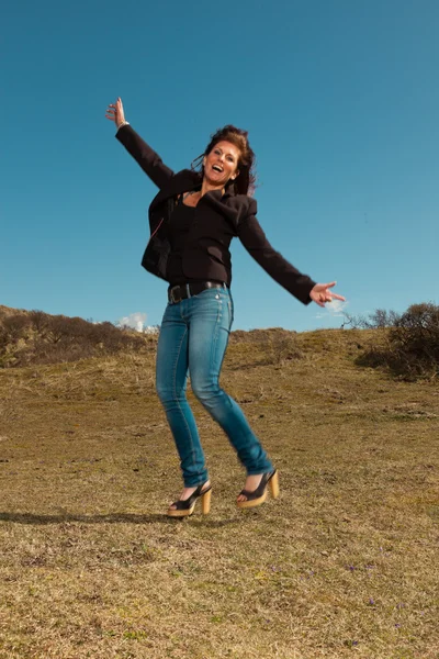 Jumping pretty brunette woman wearing brown jacket. Meadow with — Stock Photo, Image