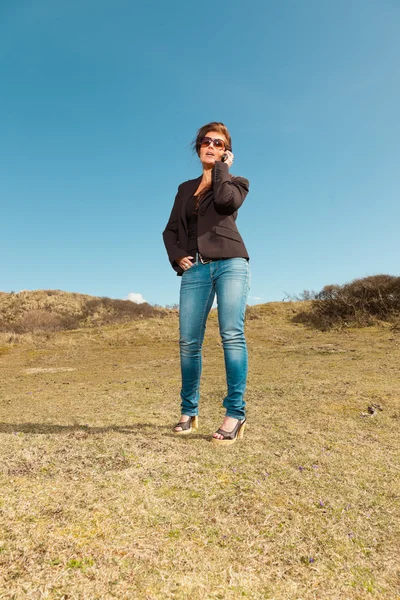 Pretty brunette woman with sunglasses using mobile phone. Meadow — Stock Photo, Image