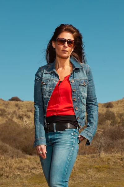 Pretty brunette woman wearing jeans and sunglasses. Meadow with — Stock Photo, Image