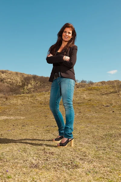 Lächelnde hübsche brünette Frau in brauner Jacke. Wiese mit — Stockfoto