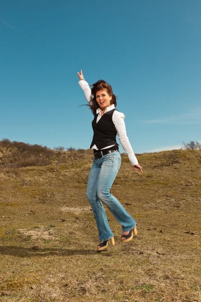 Happy pretty brunette woman wearing jeans in meadow with blue sk — Stock Photo, Image