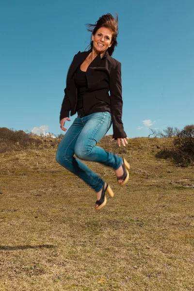 Hüpfende hübsche brünette Frau in brauner Jacke. Wiese mit — Stockfoto