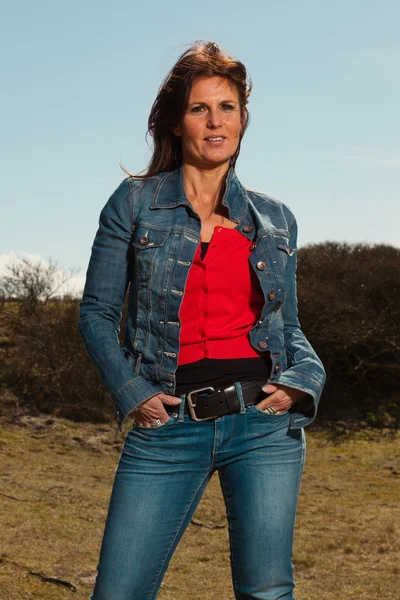 Smiling pretty brunette woman wearing jeans. Meadow with blue sk — Stock Photo, Image