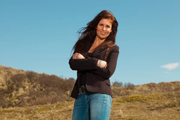 Smiling pretty brunette woman wearing brown jacket. Meadow with — Stock Photo, Image