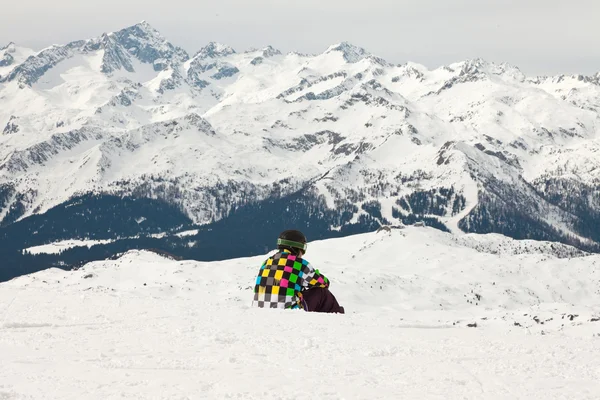 Snowboarder κάθεται στο χιόνι. τοπίο βραχώδες βουνό. — Φωτογραφία Αρχείου