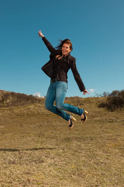 Jumping pretty brunette woman wearing brown jacket. Meadow with Royalty Free Stock Images