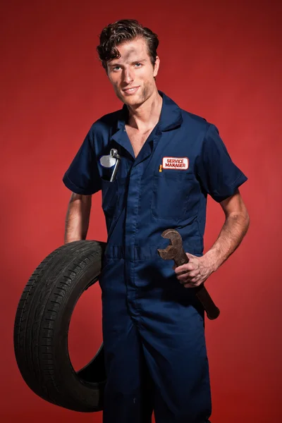 Retro fifties male car mechanic holding tool and tire. Studio sh — Stock Photo, Image