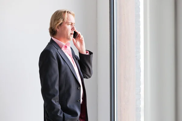 Geschäftsmann telefoniert mit Handy vor Fensterbüro. — Stockfoto