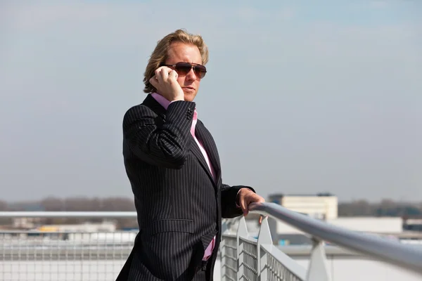 Hombre de negocios con gafas de sol llamando con teléfono celular al aire libre en r —  Fotos de Stock