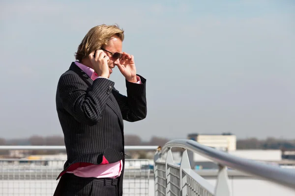 Деловой человек в солнечных очках звонит с мобильного телефона на открытом воздухе — стоковое фото
