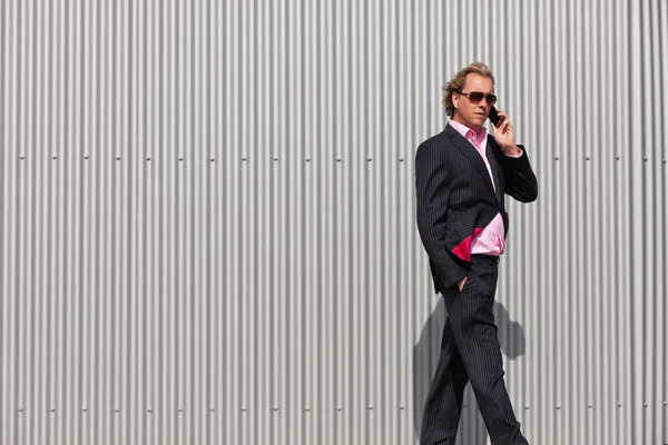 Business man with sunglasses calling near industrial wall. — Stock Photo, Image