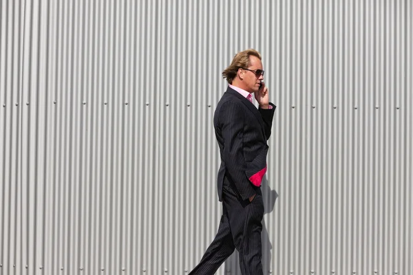 Geschäftsmann mit Sonnenbrille ruft nahe Industriemauer an. — Stockfoto