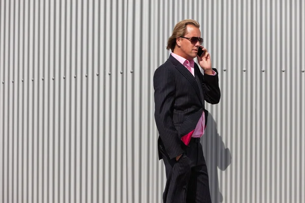 Hombre de negocios con gafas de sol llamando cerca de la pared industrial . —  Fotos de Stock