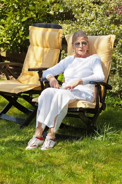 Senior woman sitting in garden. Wearing sunglasses. — Stock Photo, Image