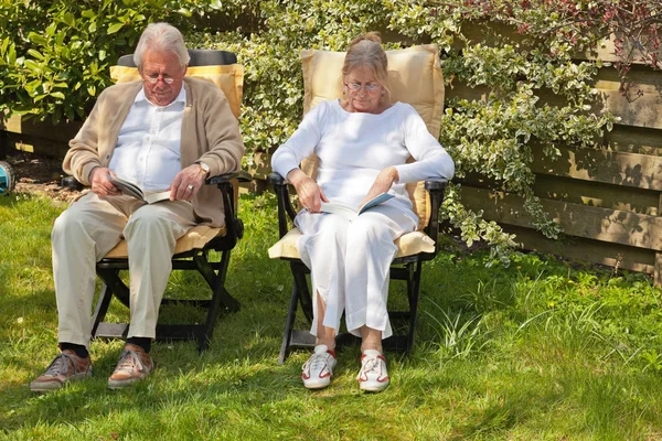 Старшая пара, сидящая в саду и читающая книгу. Летнее время . — стоковое фото