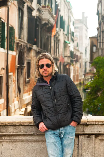 Junger Mann mit langen blonden Haaren und Sonnenbrille auf Brücke in Venedig — Stockfoto