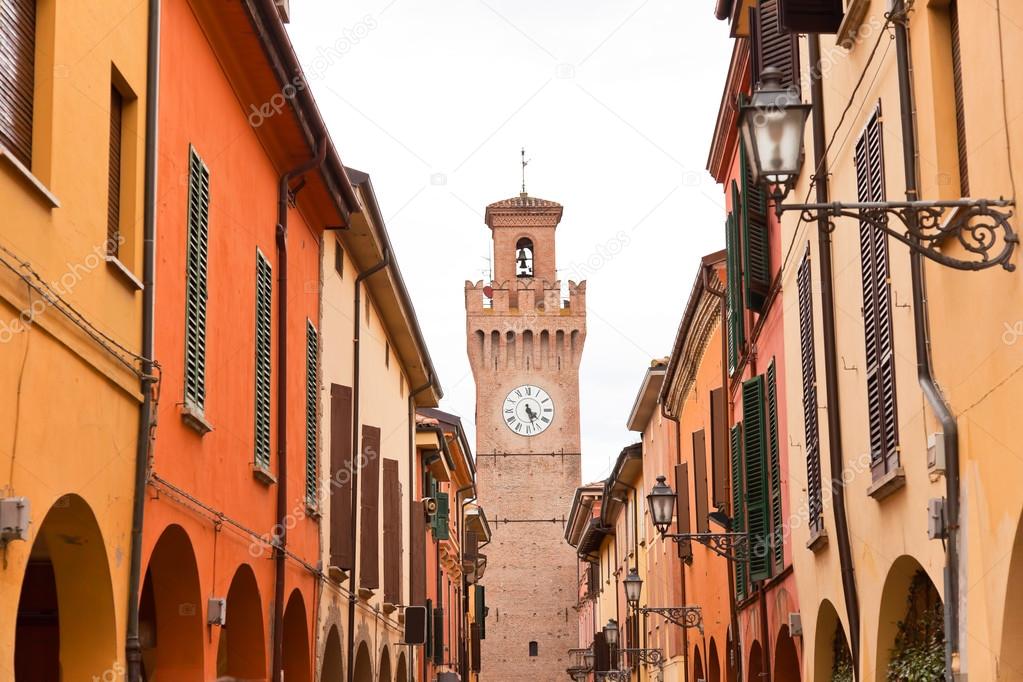 Street with houses and tower with clock in Castel San Pietro. Em