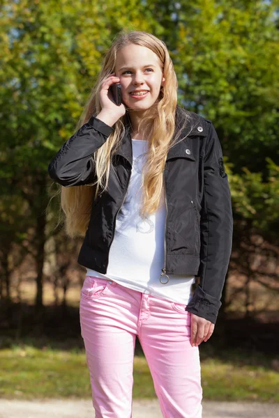 Junges blondes Mädchen mit Zahnspange im Park telefoniert mit Handy. — Stockfoto