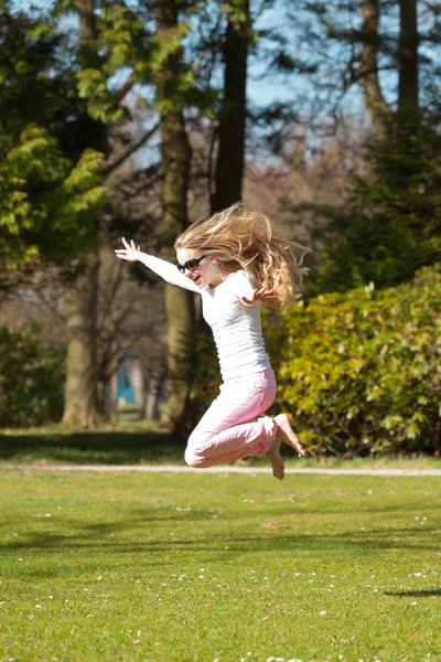 Blond flicka hoppa på fältet av gräs i parken. — Stockfoto