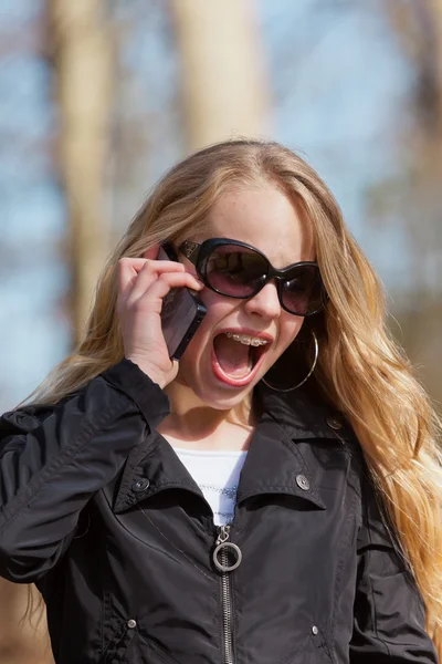 Jeune fille blonde avec des lunettes de soleil dans le parc appelant avec téléphone portable — Photo