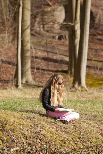 Szőke lány ül a fűben, egy könyvet olvas. szabadtéri park. — Stock Fotó