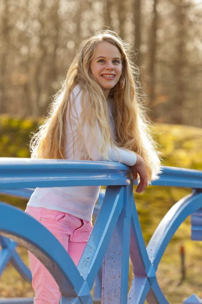 Gelukkig jong meisje met lang blond haar op brug in park. — Stockfoto