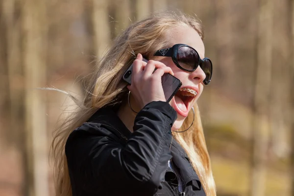 公園携帯電話を呼び出すとサングラスを持つ若いブロンドの女の子 — ストック写真