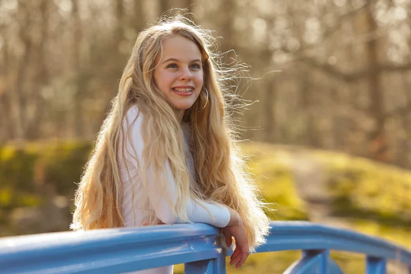 Glückliches junges Mädchen mit langen blonden Haaren auf Brücke im Park. — Stockfoto