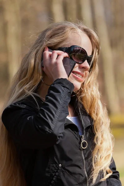Jovem loira com óculos de sol no parque chamando com celular — Fotografia de Stock